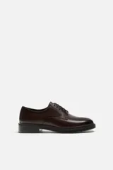 Zapato de vestir tipo derby color marrón oscuro, con parte superior lisa, horma redonda y suela a contraste.