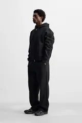 Sudadera negra relaxed fit de algodón compacto con interior en rizo, cuello con capucha ajustable, manga larga, bolsillos frontales tipo canguro, acabados en rib y cierre frontal con cremallera.