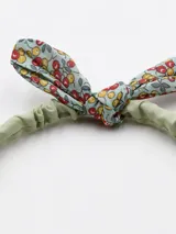 Vincha verde con moña estampada con flores rojas y amarillas.