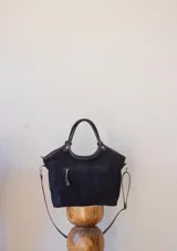 Cartera negra de gamuza con forro interior y correa larga desmontable.