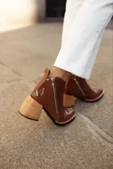 Bota corta de cuero color borgoña con textura de piel de reptil, cierre lateral con cremallera y tacón geométrico de madera clara.