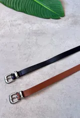 Cinto fino de cuero, disponible en color negro y marrón, con hebilla metálica plateada de estilo occidental.