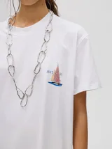 Remera blanca de corte cuadrado y holgado, con estampado pequeño de un velero en el pecho.