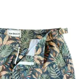 Short de baño con estampado de hojas de palmera en tonos verde, marrón y azul sobre fondo azul oscuro. Tiene pretina fija con hebillas metálicas laterales para ajustar, botón a presión y cierre frontal. Incluye tres bolsillos (dos laterales y uno trasero).