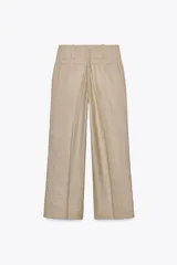 Pantalón de tiro alto color beige, con bolsillos delanteros y falsos bolsillos traseros. Pierna ancha y cierre frontal con ganchos metálicos y botones.