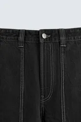 Pantalón relaxed fit de denim negro con costuras blancas en contraste, bolsillos frontales y traseros de parche, cierre frontal con cremallera y botón.