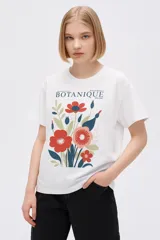 Remera blanca con estampado de flores rojas, azules y verdes, con texto "Botanique" en la parte superior.