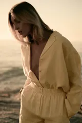 Camisa de lino color amarillo claro, de corte recto, con cuello solapa, escote en pico, cierre frontal con botones y mangas largas con puños abotonados.