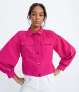 Campera color fucsia de crepe con cuello de camisa, manga abullonada, cierre frontal con botones y bolsillos frontales aplicados.