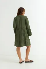 Vestido corto color azul marino, de manga larga con volado en el puño y corte en capas con volados en el cuerpo. Presenta cuello en V con botones frontales.