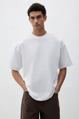 Remera blanca de algodón de peso medio, con cuello redondo ribeteado, hombros caídos y bajo recto. Corte oversized.