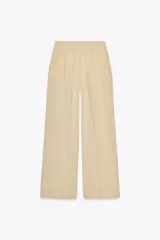 Pantalón color beige de lino, de tiro alto, con pinzas delanteras, bolsillos frontales y pernera ancha.