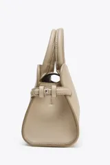 Bolso mini city color beige con doble asa de mano y asa bandolera extraíble. Tiene detalles laterales, pespuntes en el cuerpo y cierre con solapa y botón imantado.