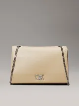 Cartera tipo sobre de piel sintética color beige claro, con solapa frontal y herrajes plateados. Presenta el monograma 'CK' en metal en la parte frontal y una correa de cadena convertible que permite usarla al hombro o cruzada.