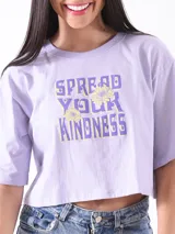 Remera corta lila con estampado de texto 'Spread Your Kindness' con flores amarillas.