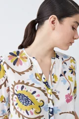 Camisa blanca con estampado floral en tonos azul, amarillo, rosa y marrón. Tiene cuello mao, mangas cortas abullonadas y cierre frontal con botones.