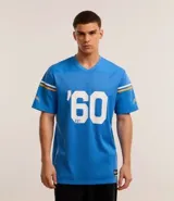 Remera deportiva celeste con cuello en V y mangas cortas con rayas blancas y doradas. Estampado frontal con el número '60' y el texto 'EST.' en blanco.