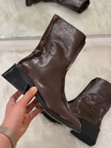 Botas cortas color chocolate con textura de cocodrilo, punta cuadrada y tacón bajo. Cuentan con cierre lateral.