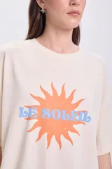 Remera manga corta oversize color crudo con estampa de sol y texto 'Le Soleil' en naranja y celeste.