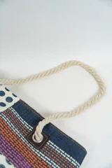 Bolso de playa o tote bag con diseño de patchwork en tonos rosados, naranjas y blancos. Presenta secciones con estampado de lunares rojos y secciones con tejido de rafia. Las asas son de cuerda trenzada.