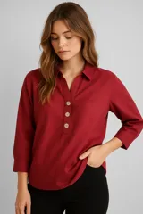 Blusa color borgoña de poliéster, corte holgado, con cuello camisero, mangas 3/4 y cierre frontal parcial con botones de madera.