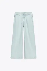 Pantalón de jean celeste claro, de tiro alto y corte wide leg. Tiene bolsillos delanteros y traseros, cierre frontal con cremallera, botón y cordones.