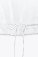 Camiseta blanca de algodón con cuello redondo, mangas cortas y bajo asimétrico ajustable con lazadas.