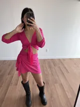 Conjunto de top manga larga con nudo frontal y falda corta cruzada con lazo lateral, color fucsia.
