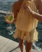 Minivestido color crema con cuello halter, espalda descubierta y falda con volados.