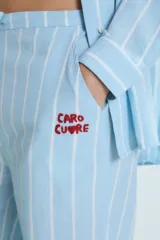 Conjunto de pijama celeste a rayas verticales blancas, compuesto por una camisa de manga larga con cuello mao y botones, y un pantalón de corte recto. La camisa y el pantalón tienen bordados de corazones, soles y otros motivos.