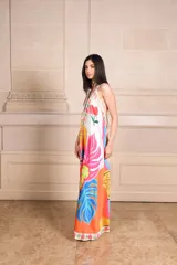 Vestido largo de seda con estampado vibrante y multicolor que incluye motivos frutales y caras sonrientes. Diseño de solera con escote halter anudado al cuello y falda amplia.