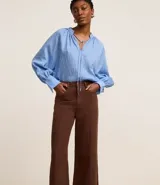 Pantalón wide leg de sarga color marrón chocolate, con cintura alta, trabillas, bolsillos delanteros y traseros, cierre con botón y cremallera, y costura vertical delantera.