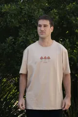 Remera celeste de manga corta con cuello redondo y estampado de tres hongos rojos con lunares blancos y la palabra 'Tuya' debajo.