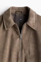 Campera marrón con cuello clásico y cierre frontal. Tiene bolsillos insertados al bies con botón a presión, bolsillo interior y botón en los puños. Corte estándar y forro interior.