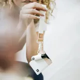 Llavero de muñeca con cinta de tela color crudo, detalle de cuero sintético color rosa con logo grabado y gancho metálico plateado.