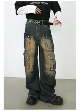 Pantalón de jean ancho (baggy) con lavado oscuro y efecto desgastado en tonos marrones/ocre. Presenta múltiples bolsillos cargo grandes con tapa y botones a presión en las piernas.