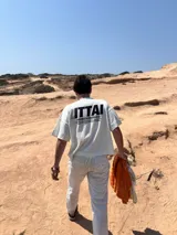 Remera color crema de corte recto y mangas cortas, con estampado en la espalda con el logo "ITTAI" en negro con líneas rojas, azules y blancas, y la leyenda "AN IBIZA PRODUCE. Ittai Stars Department Gallery - Ibiza Edition. If you're in Ibiza, 112 is not an option.".