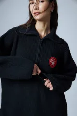Sweater negro de cuello polo tejido con cierre diente de perro a tono y tajos laterales. Tiene un parche bordado con elementos del drop.