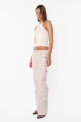 Pantalón cargo color arena de corte recto y tiro bajo, con recortes y presillas dobles en la cintura. Tiene acceso mediante cierre de nylon y botón personalizado, seis bolsillos laterales y dos en la espalda con tapa y botón snap a presión.