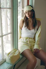 Bermuda corta tipo pijama con rayas verticales amarillas y blancas, tiro alto, cintura elástica ajustable con lazo y detalle de botones decorativos en el frente.