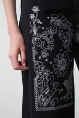 Pantalón de denim azul oscuro con bordado estilo bandana en blanco en los laterales de las piernas y en los puños. El corte es recto y amplio, llegando al tobillo.