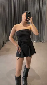 Minivestido negro ajustado al cuerpo, sin mangas y con escote recto. Presenta frunces laterales con lazos ajustables.