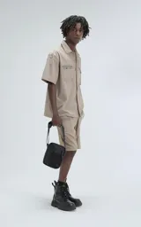 Camisa beige de manga corta, estilo técnica, confeccionada en microfibra liviana. Con doble bolsillo frontal y broches en lugar de botones.