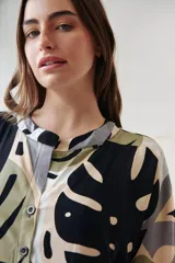 Vestido camisero midi con estampado de hojas en tonos negro, verde, gris y beige. Tiene cuello camisero, mangas cortas y cierre frontal con botones.
