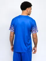 Remera deportiva azul con el escudo del Club Nacional de Football en el pecho y diseño de cuadros rojos y blancos en las mangas.