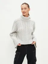 Polerón de tejido de punto color gris claro, con cuello alto y diseño de trenzas en el cuerpo y mangas. Corte holgado y puños anchos.