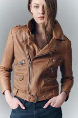 Campera negra de cuero ovino, estilo rocker, con cinturón, charreteras y solapas. Tiene cierres y detalles metálicos en frente y espalda.