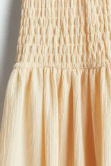 Vestido largo color crema, sin mangas, con cuerpo fruncido y falda con leve vuelo.