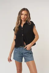 Camiseta negra con textura acanalada, corte holgado y cuadrado, cuello en punta, bolsillos amplios y botones funcionales.