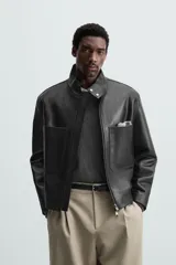 Cazadora cropped de piel negra, con cuello alto, cierre frontal con cremallera, bolsillos de parche en el pecho y puños con botón.